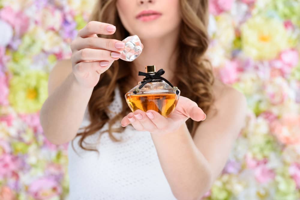 A woman holding and opening a bottle of sweet perfumes, floral background suggesting scent variety and personal expression.